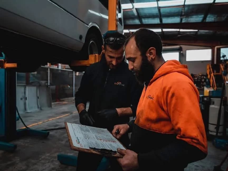 Two Skylight Bus Lines mechanics working through a maintenance checklist beneath a raised coach